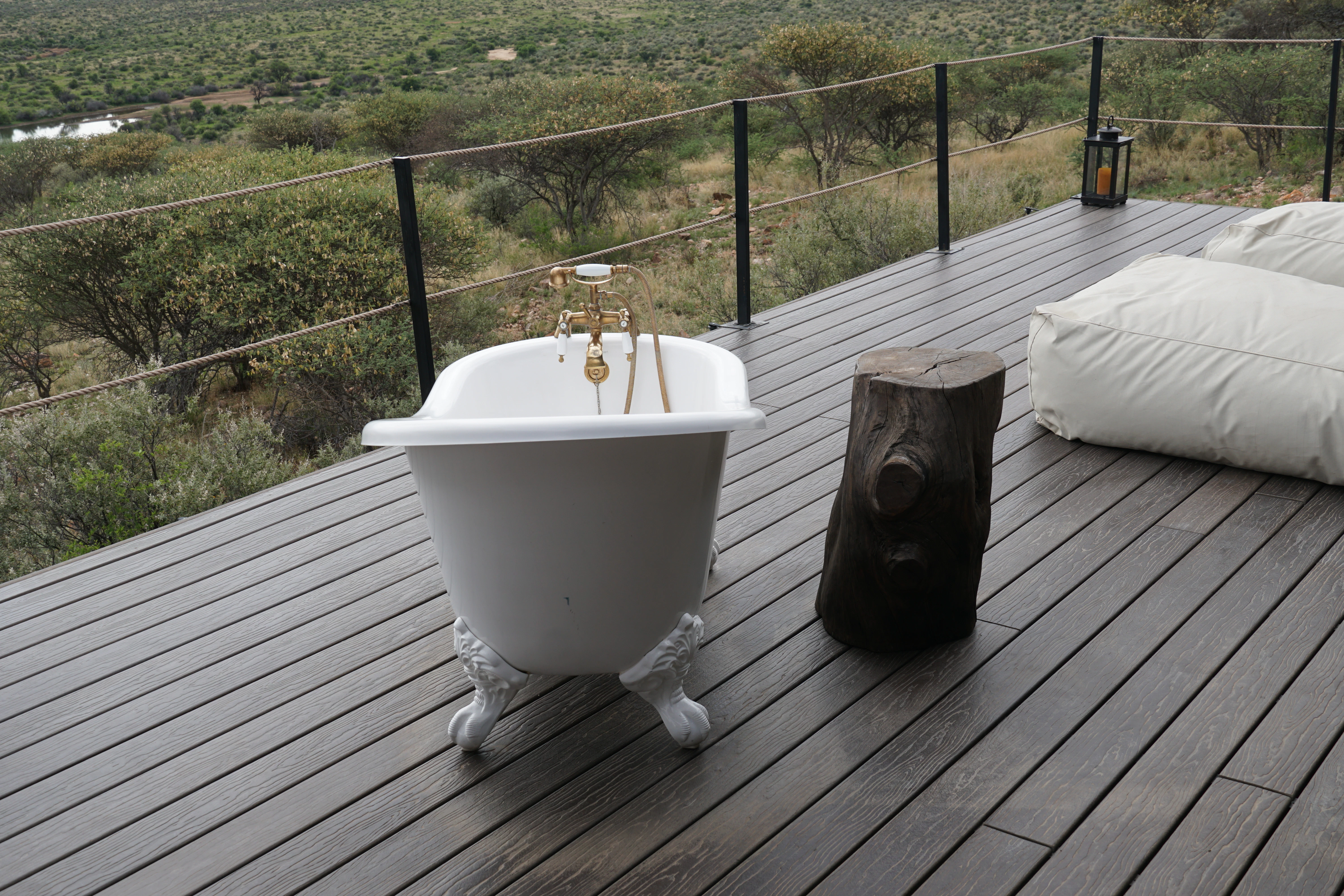 Bathtub on a wooden deck overlooking savanna landscape.