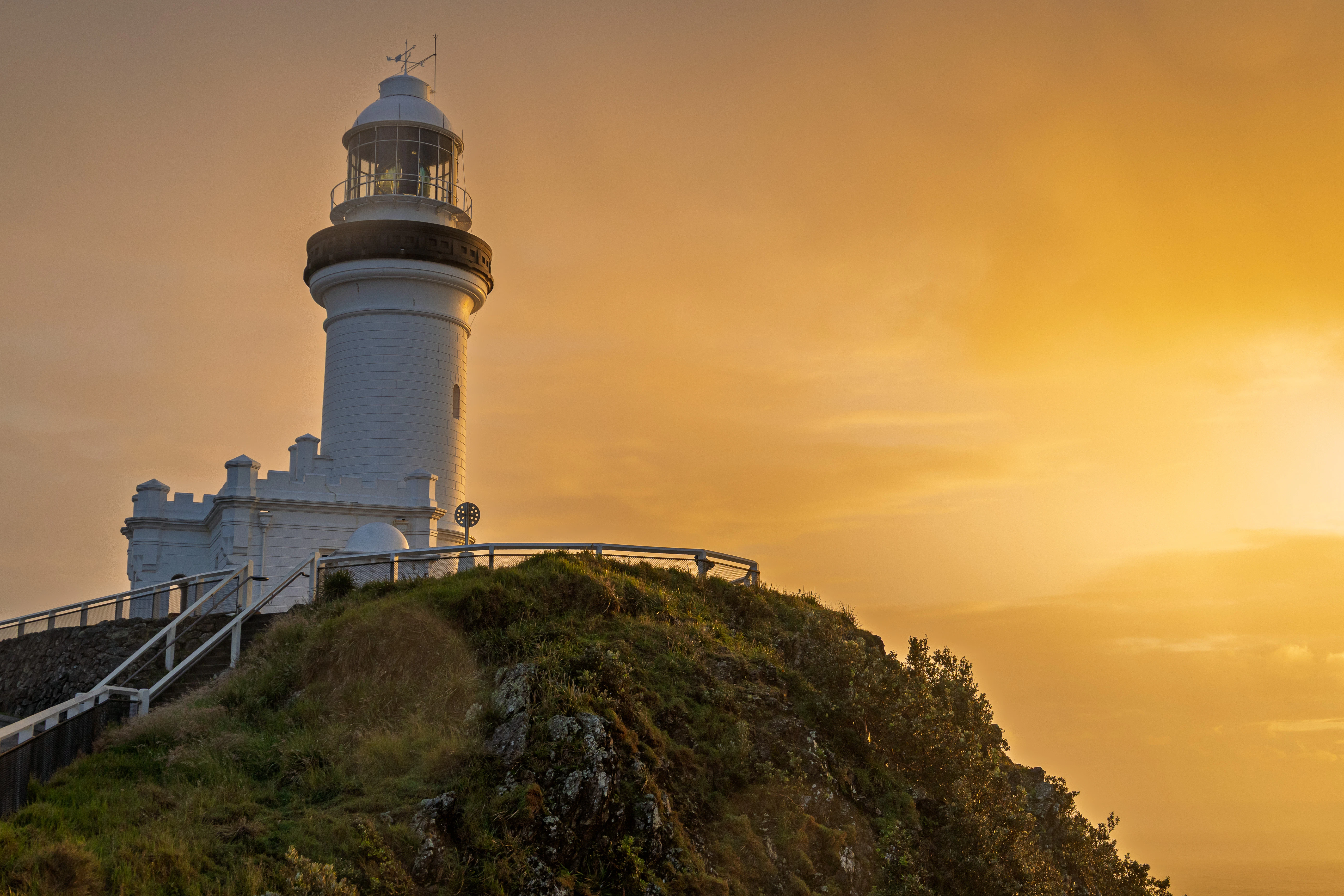 A lighthouse stands on a hill at sunset.