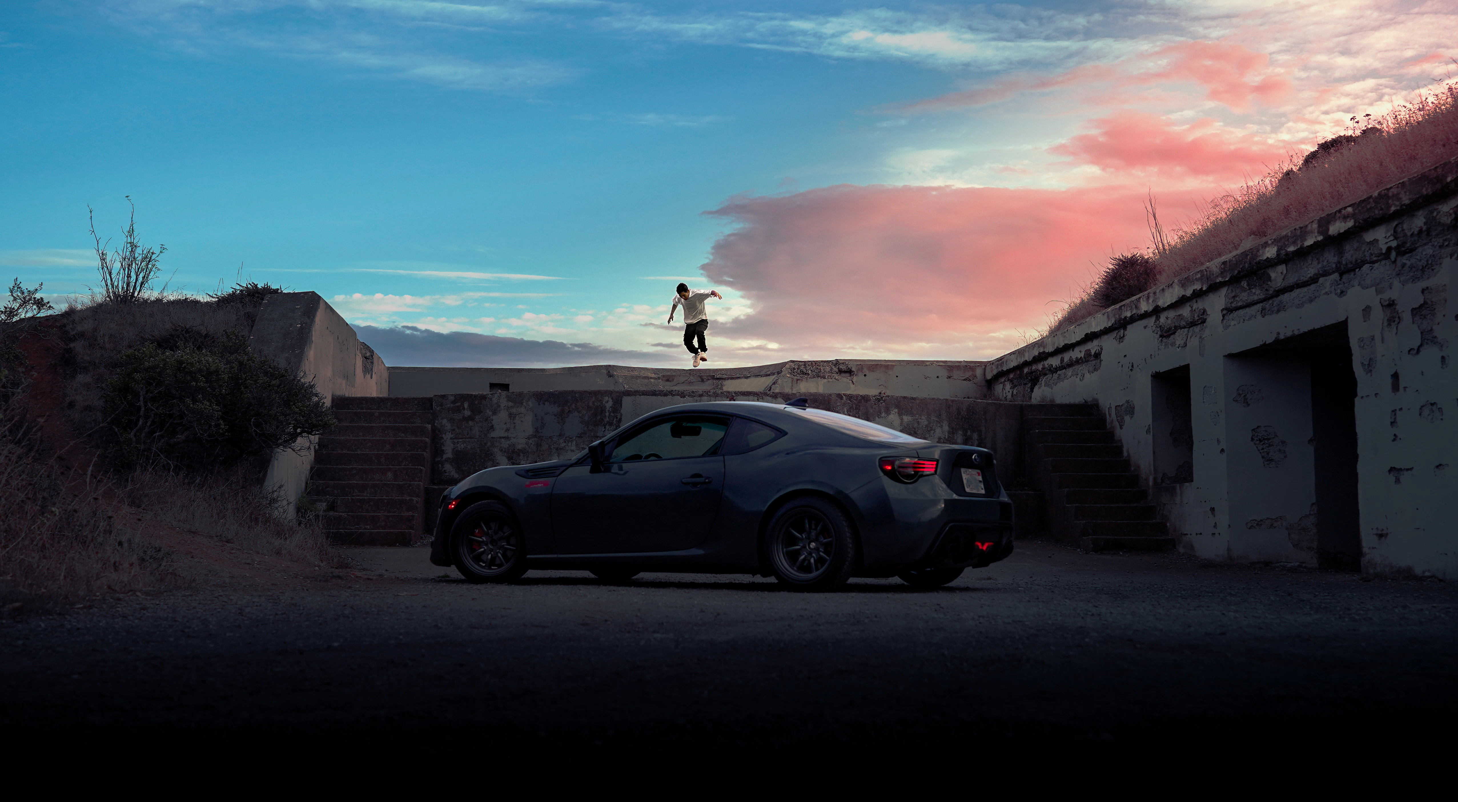 Man standing on wall near dark car at sunset