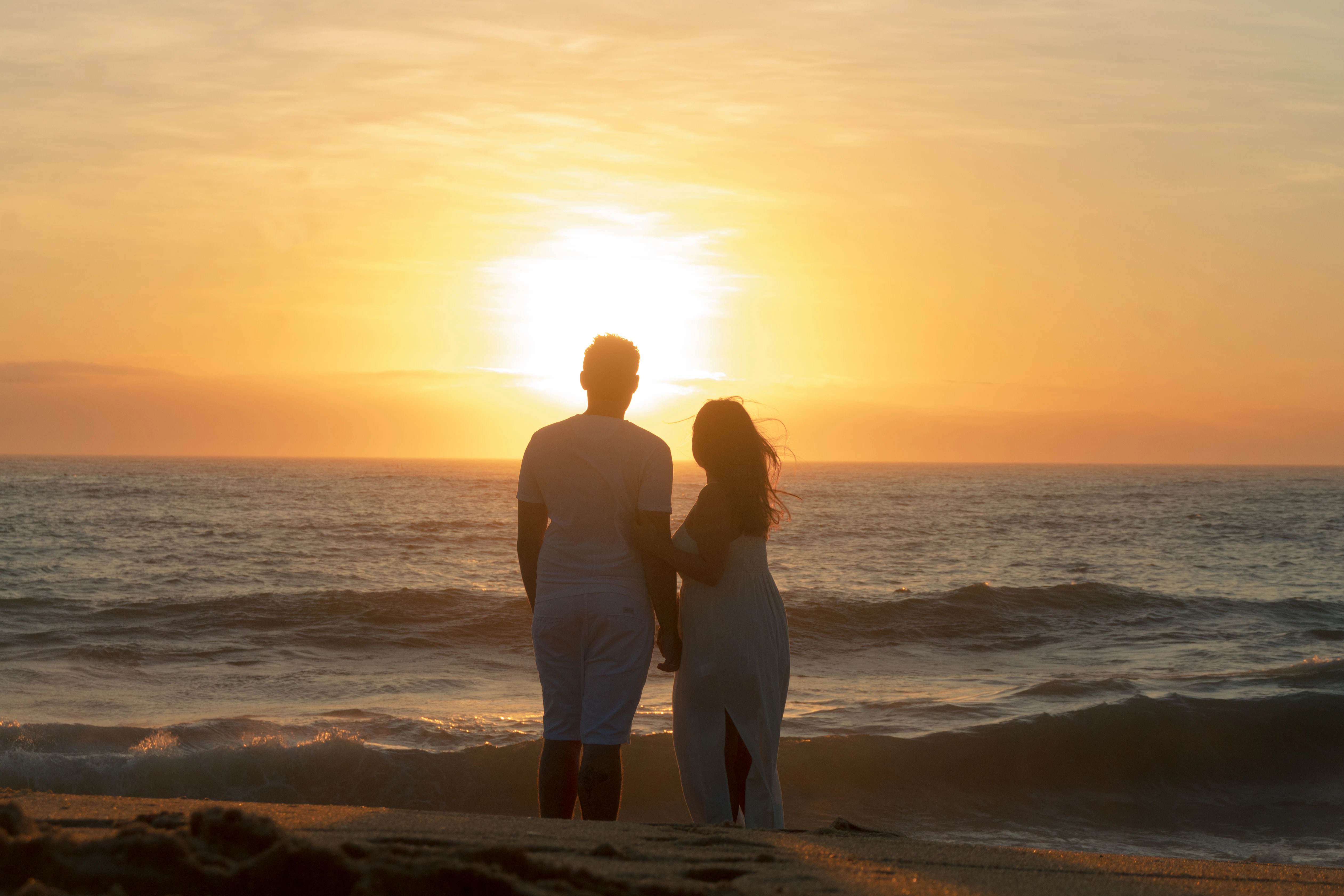 Couple holding hands watching sunset over the ocean