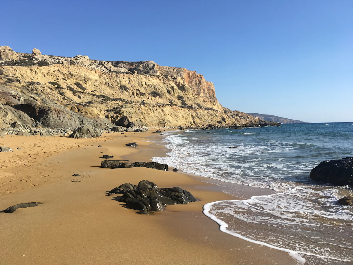 a sandy beach next to a rocky cliff