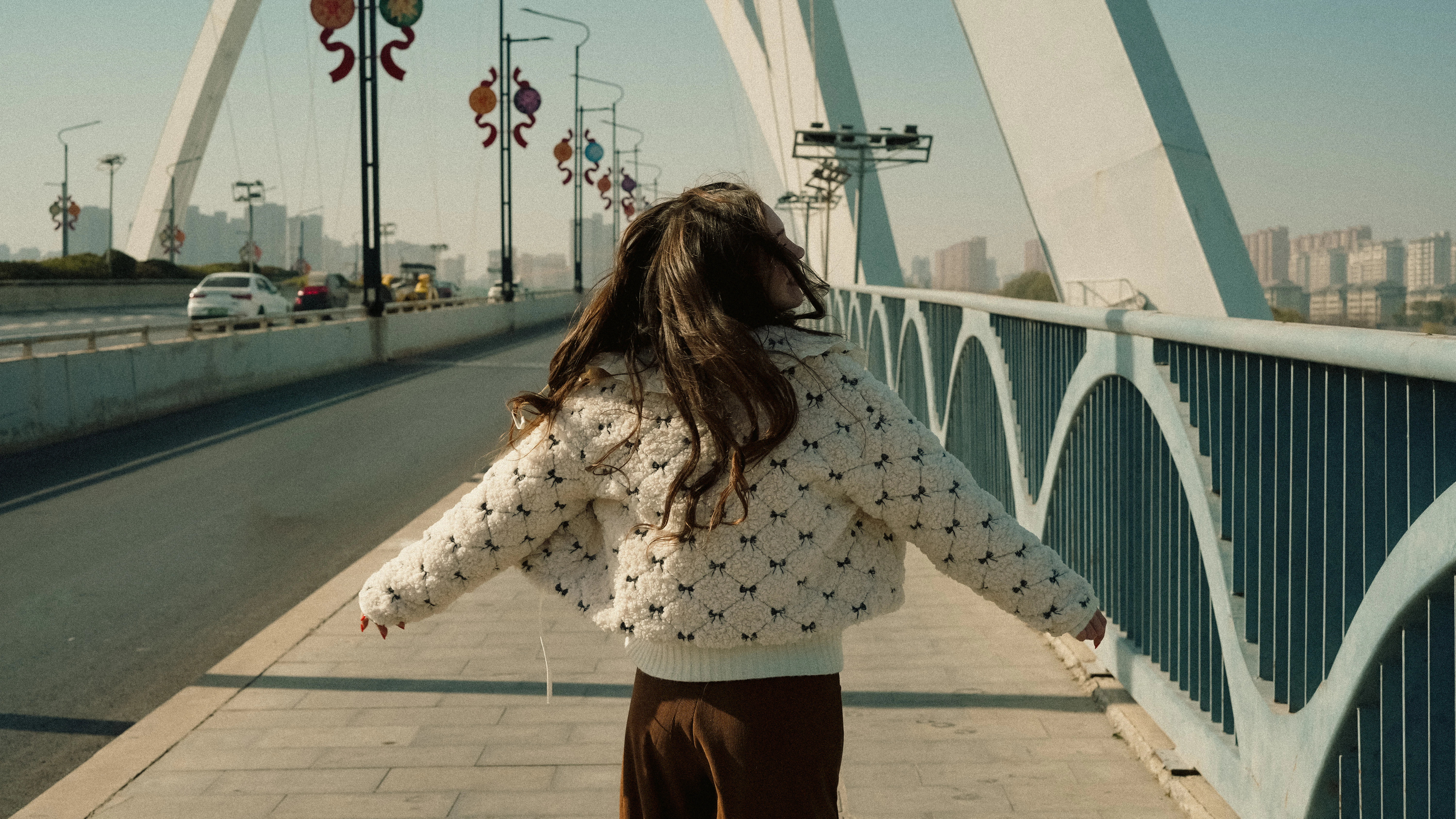 A young girl with long hair walks on a bridge.
