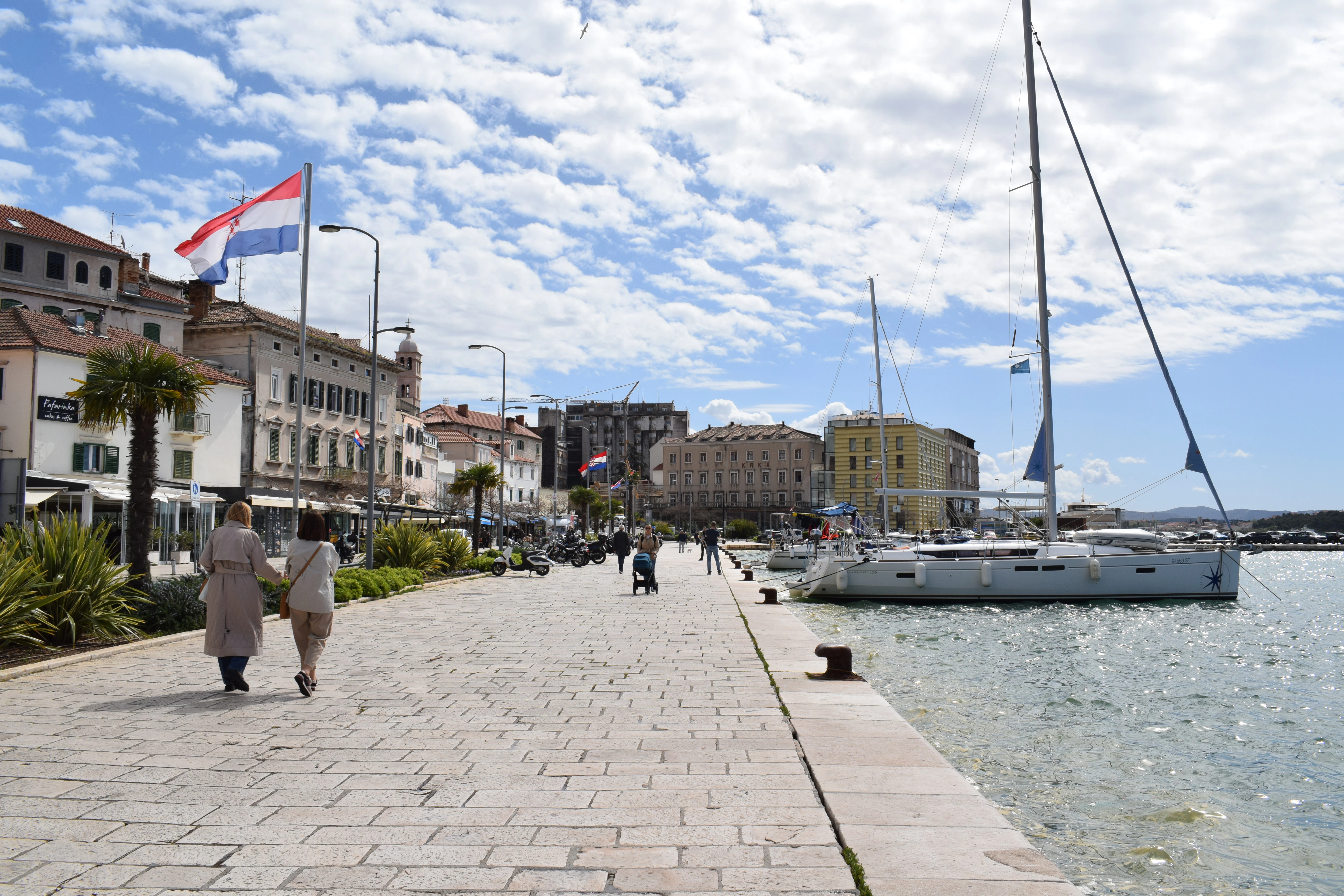 a couple of people walking down a sidewalk next to a body of water