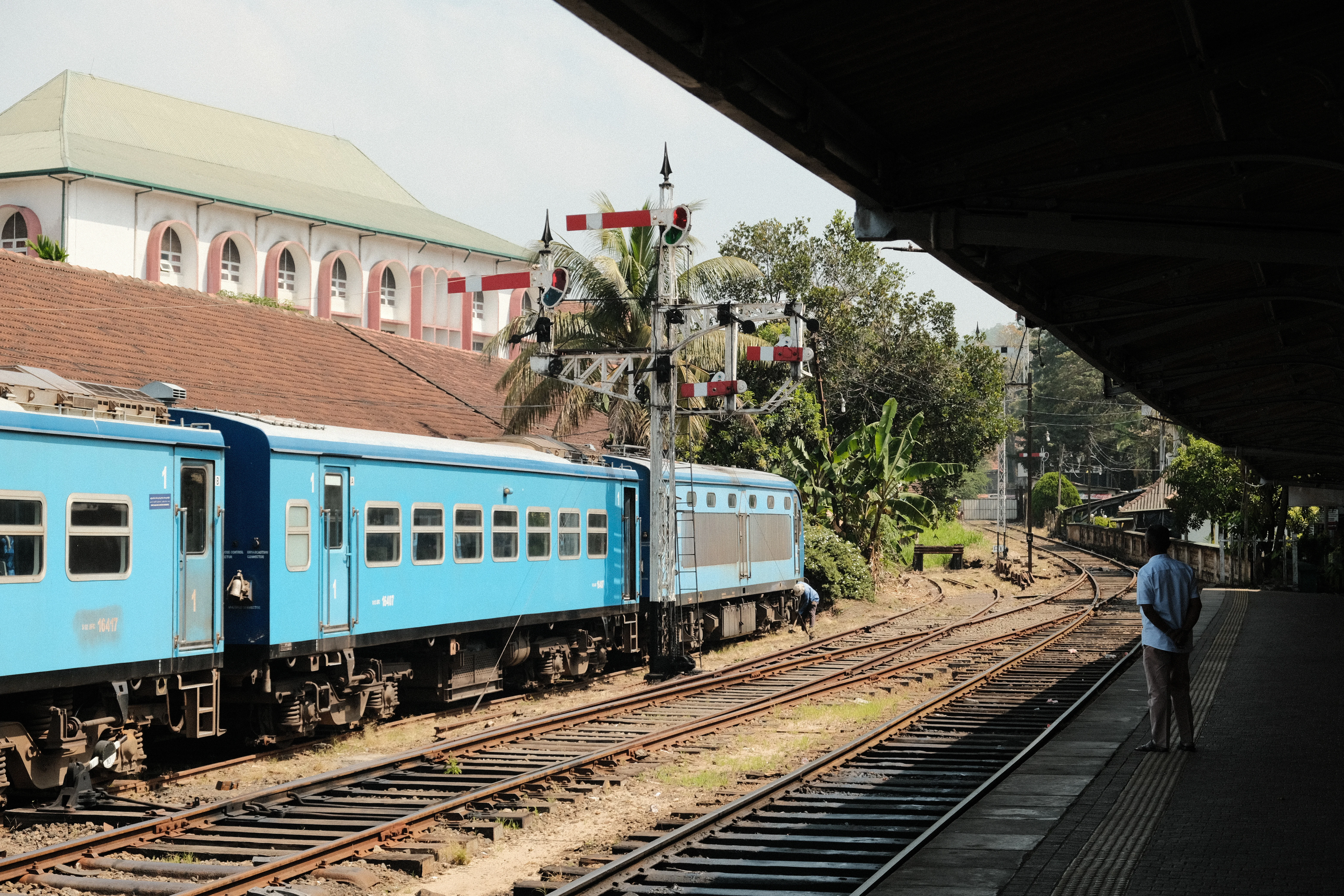 a blue train traveling down train tracks next to a train station