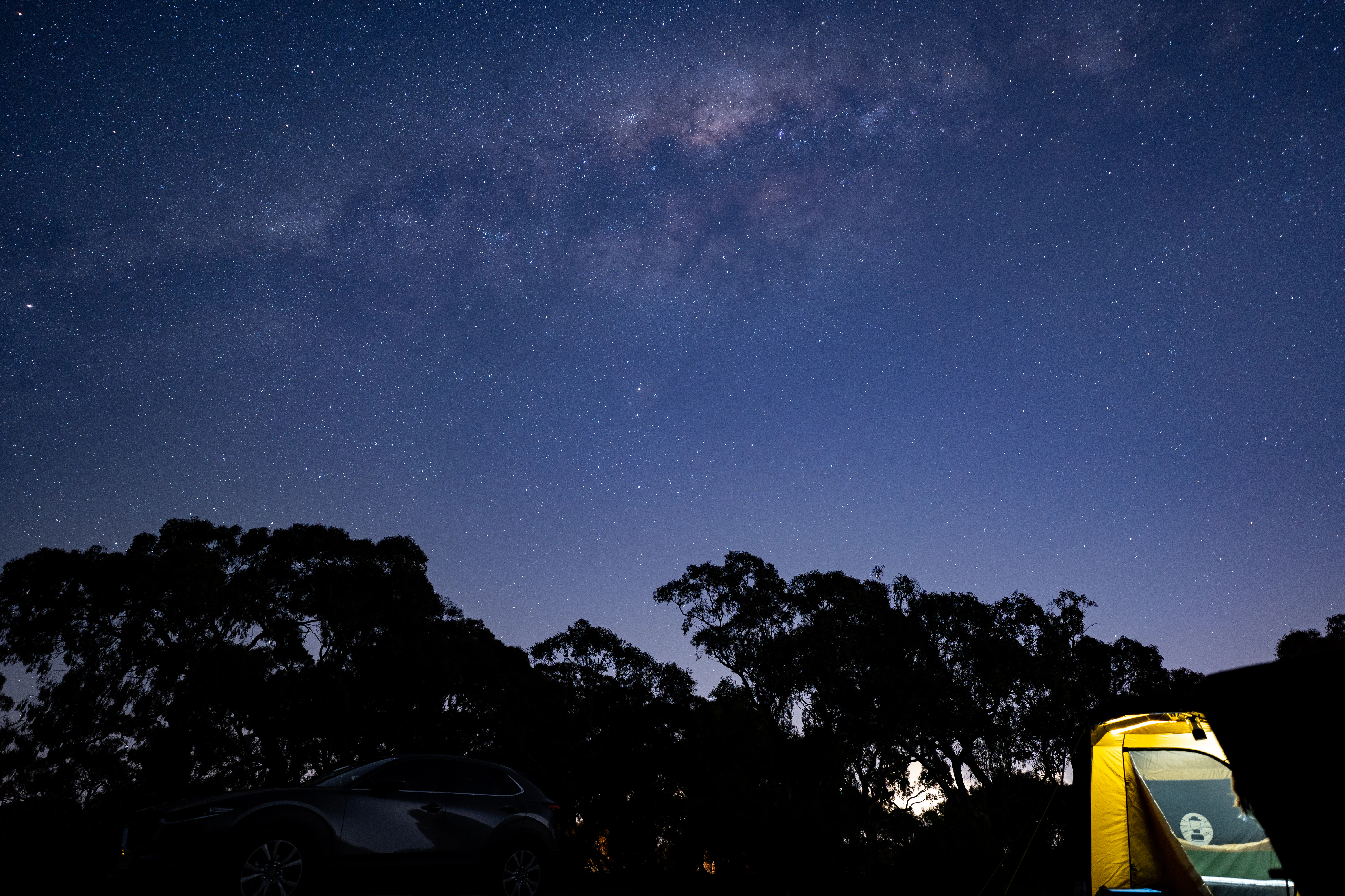 the night sky with stars and a car parked in the foreground