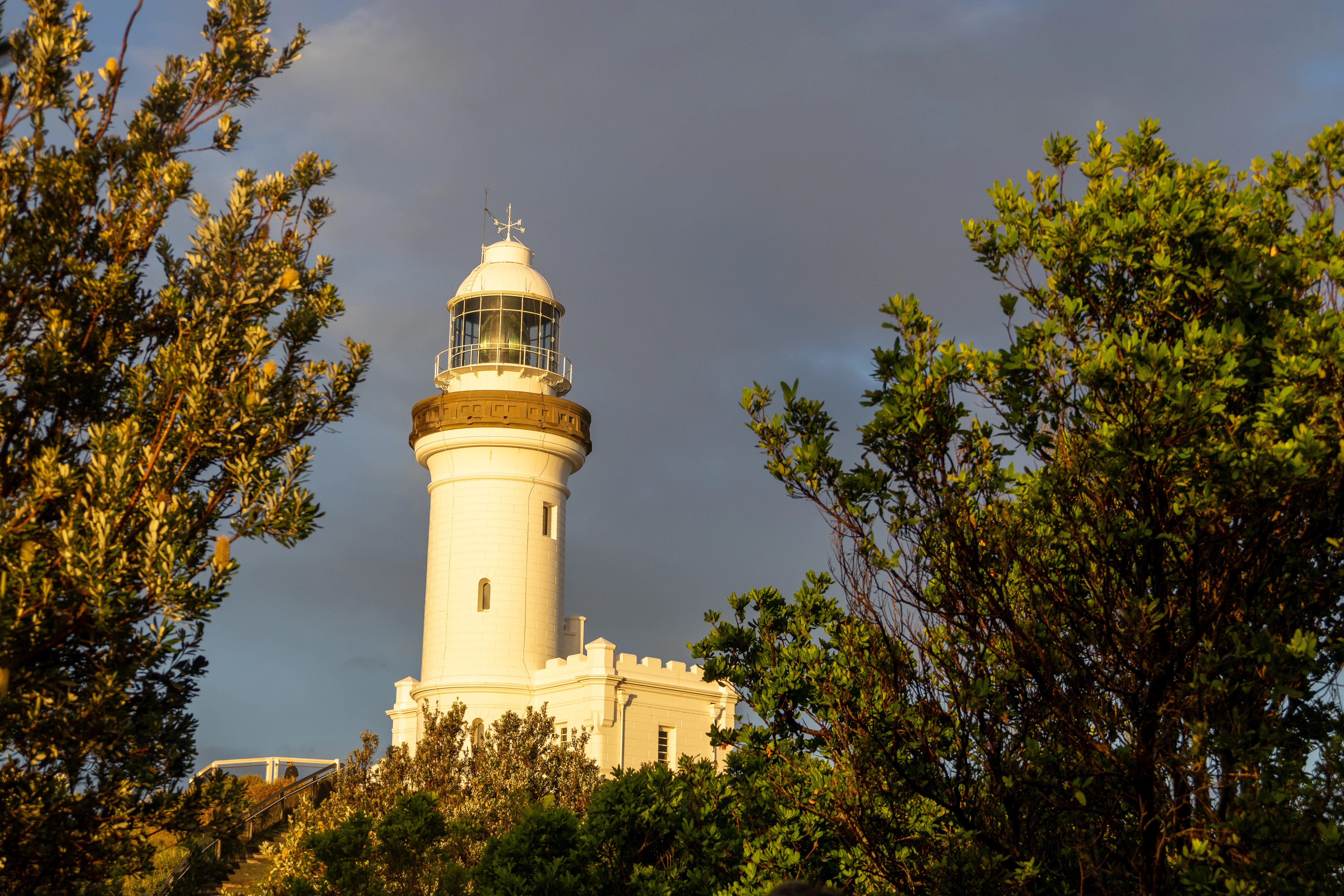 White lighthouse surrounded by green trees under cloudy sky