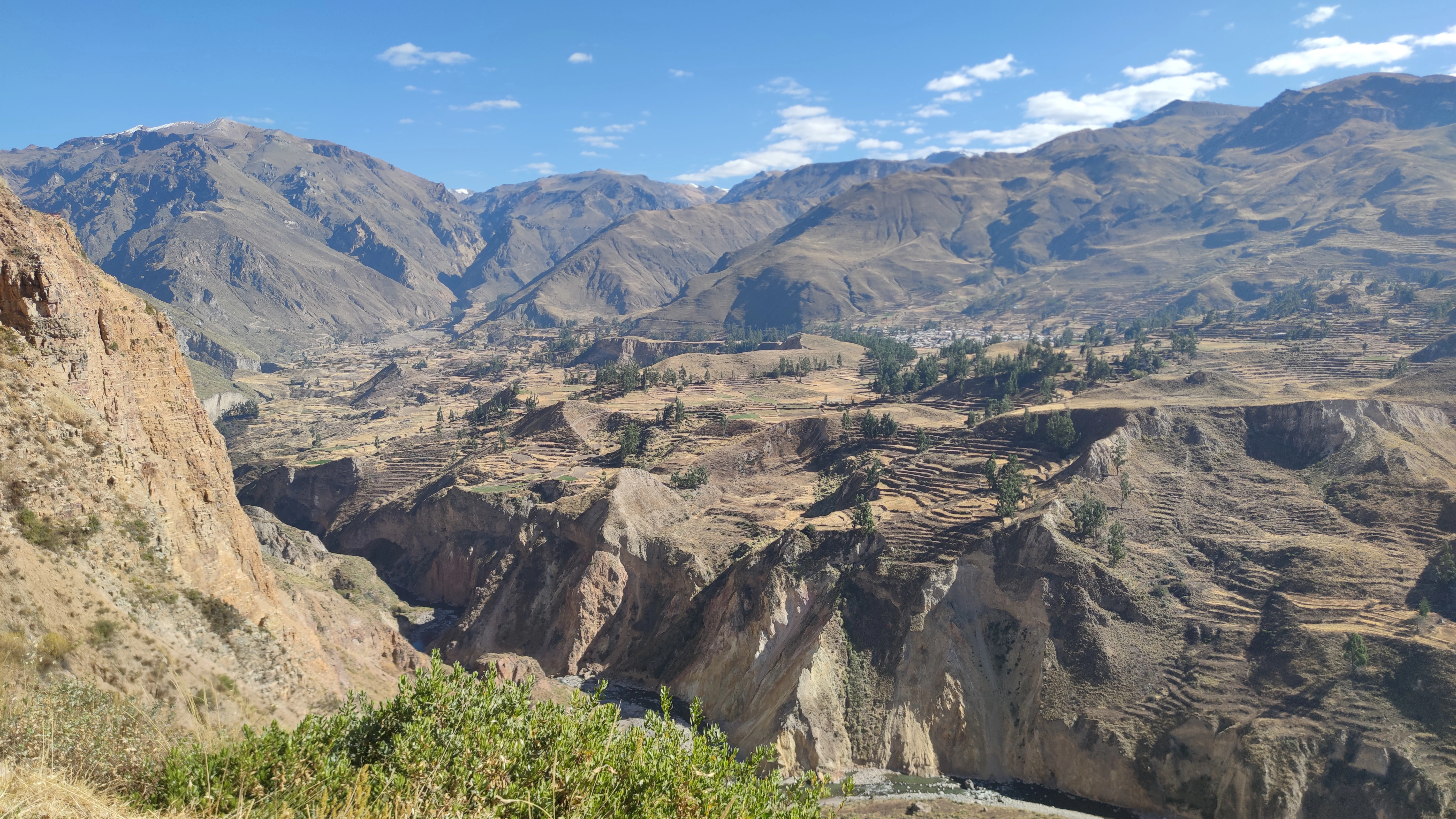 Arid mountain valley with steep, eroded slopes under blue sky.