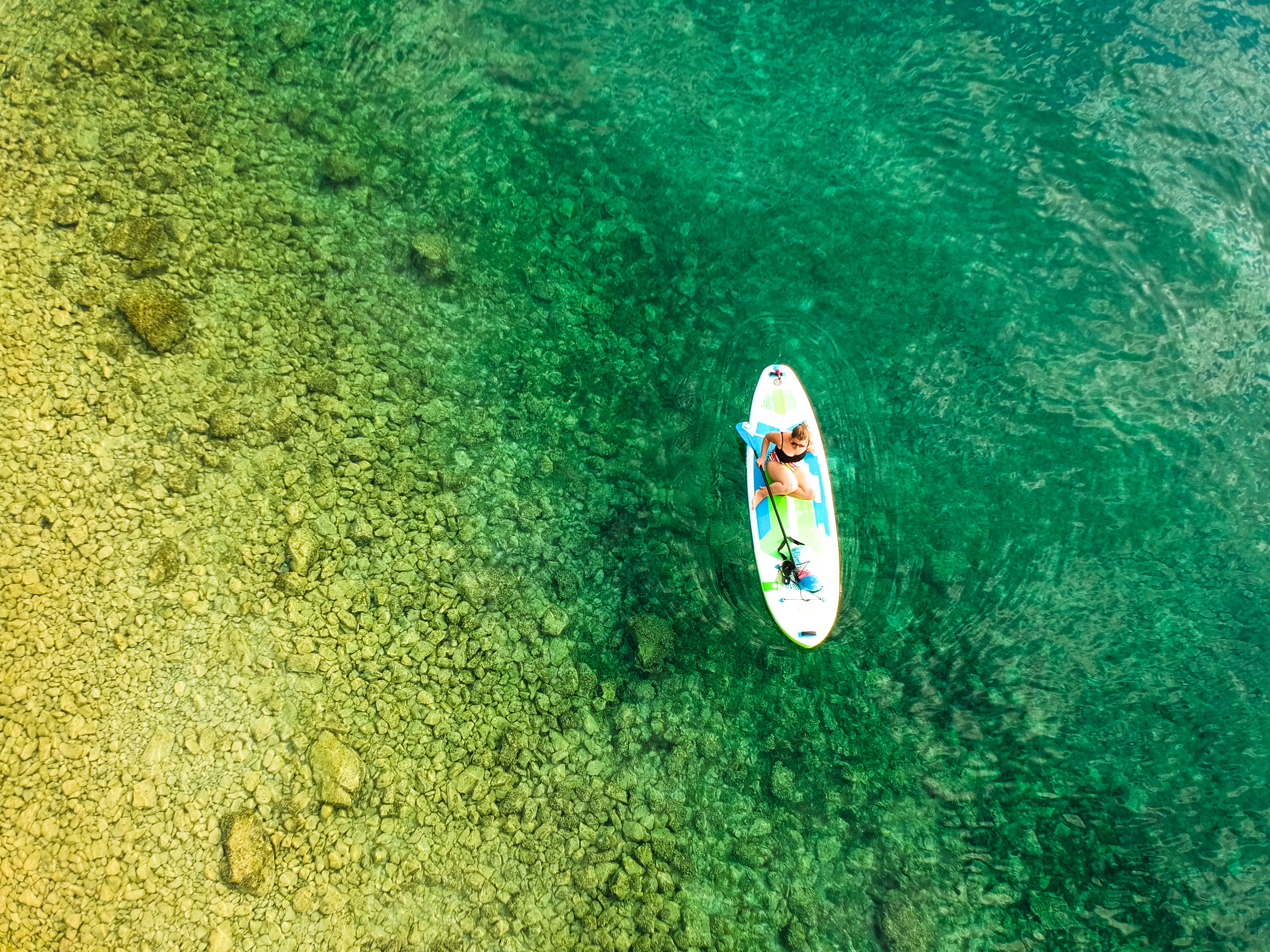 Woman paddleboarding on clear turquoise water over rocks