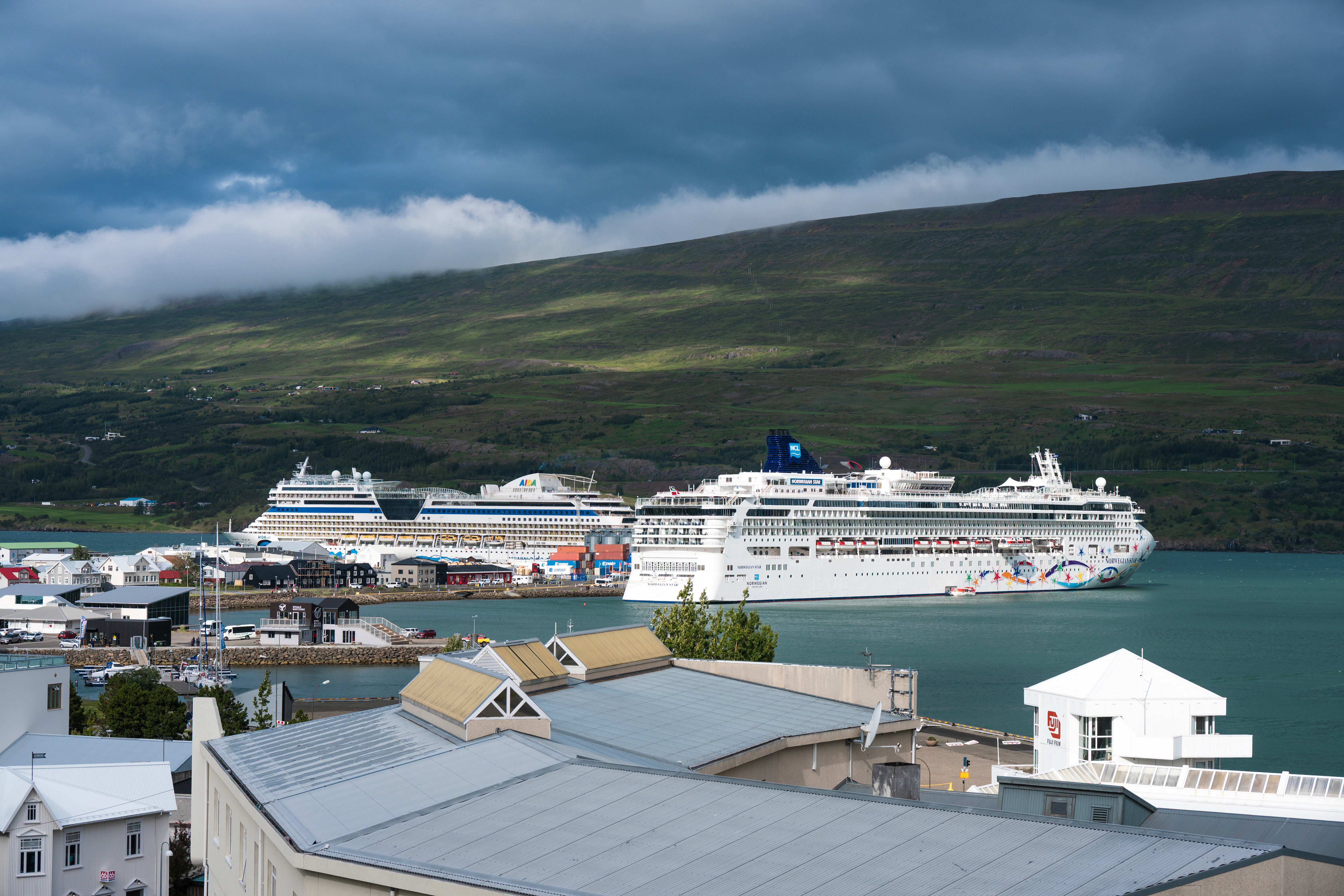 Two cruise ships docked in a harbor with mountains behind.
