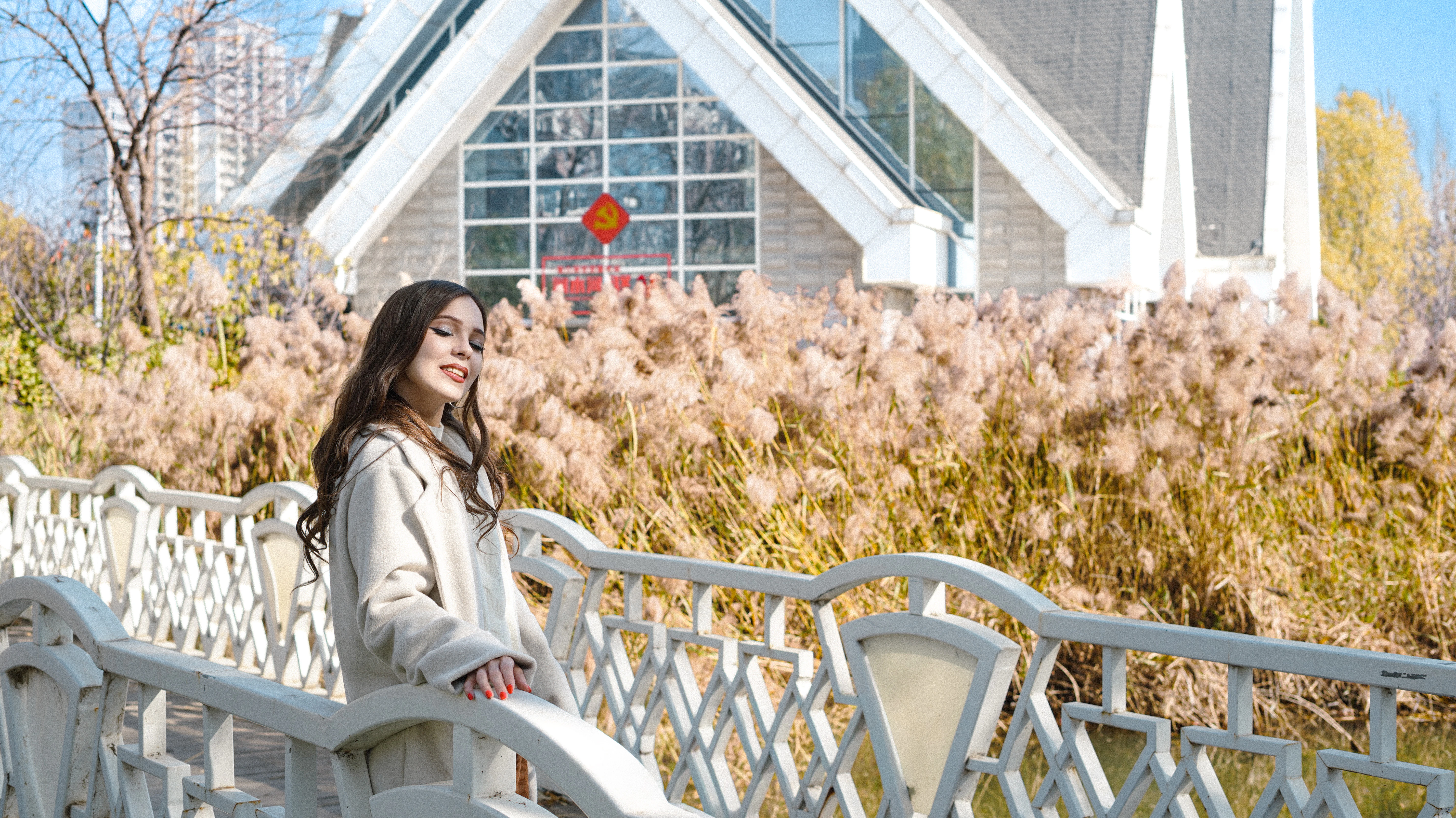 Woman standing on a bridge with tall grass and building.